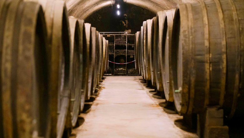 Historischer Keller, © Sektkellerei Inführ Ein historischer Weinkeller mit großen Holzfässern auf beiden Seiten eines schmalen Ganges.