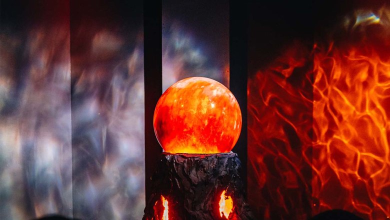 Vulkankugel, © Kuchlerhaus GmbH Leuchtende Kugel auf einem dunklen Sockel in einem Raum mit feurigen Lichtreflexionen.