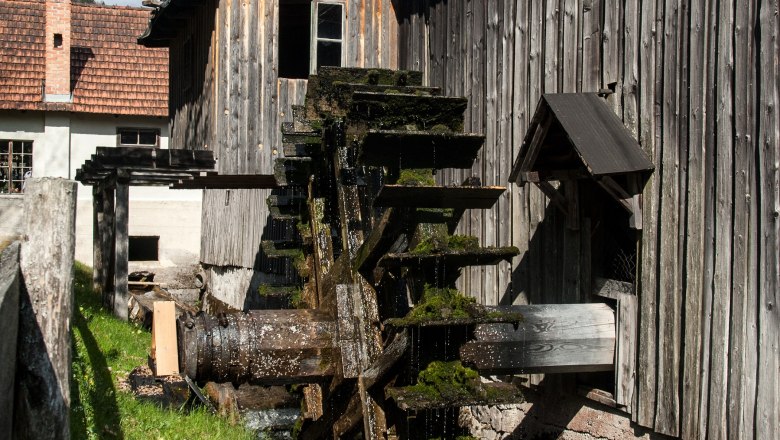 Waldbauernmuseum, © Corinna Pernitsch Ein altes Wasserrad an einem Holzgebäude im Freilichtmuseum bei sonnigem Wetter.