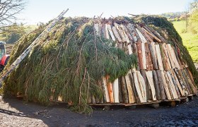 Ein traditioneller Kohlenmeiler aus Holz und Zweigen auf einem Feld.
