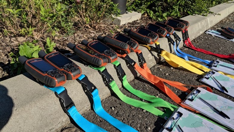 Mehrere GPS-Ger&auml;te mit bunten B&auml;ndern liegen auf dem Boden neben Klemmbrettern mit Karten.