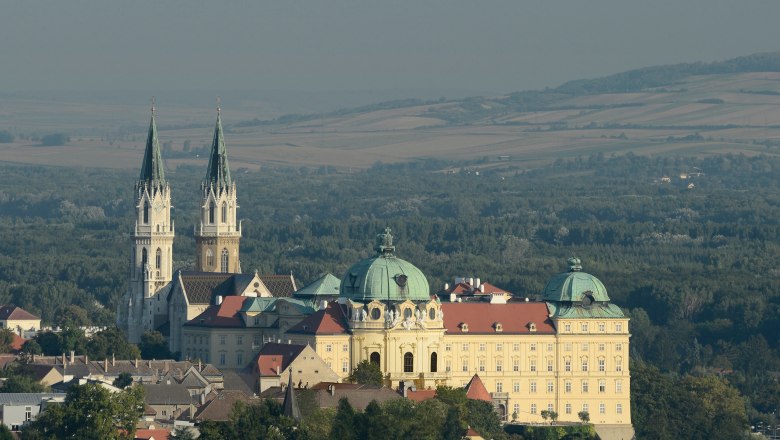 Luftaufnahme des Stifts Klosterneuburg mit zwei Kircht&uuml;rmen und umliegender Landschaft.