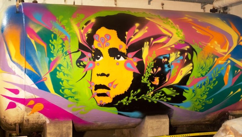 Graffiti auf einem Tank mit buntem Gesicht und Pflanzenmotiven.