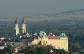 Luftaufnahme des Stifts Klosterneuburg mit zwei Kircht&uuml;rmen und umliegender Landschaft.