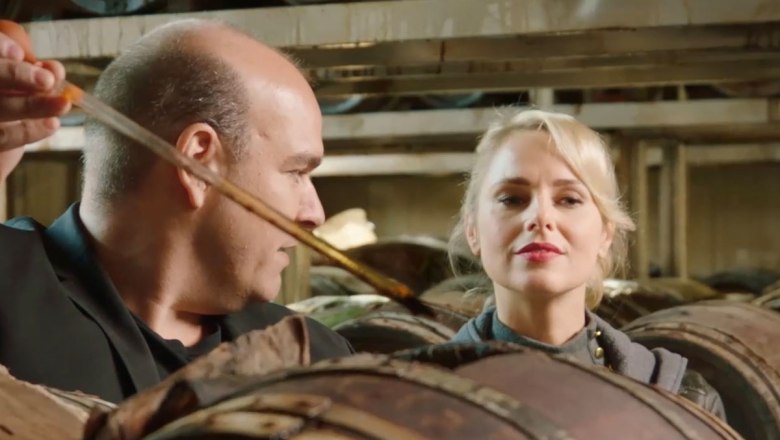 Zwei Personen in einer Balsamico-Kellerei, umgeben von Holzf&auml;ssern.