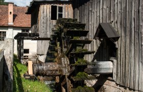Ein altes Wasserrad an einem Holzgeb&auml;ude im Freilichtmuseum bei sonnigem Wetter.