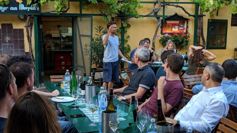 Gruppe von Menschen bei einer Weinverkostung im Freien, ein Mann spricht zu den Teilnehmern.