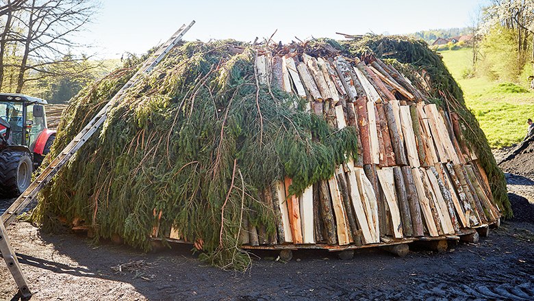 Ein traditioneller Kohlenmeiler aus Holz und Zweigen auf einem Feld.