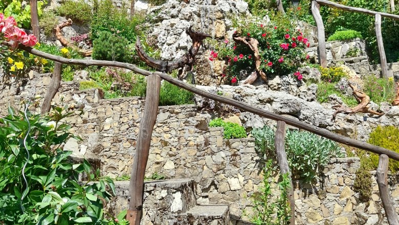 Steingarten mit Blumen, Holzgeländer und Hund.