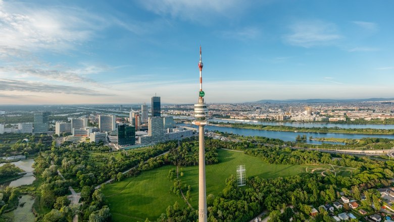 Luftaufnahme des Donauturms in Wien mit umliegender Stadtlandschaft und Donau.