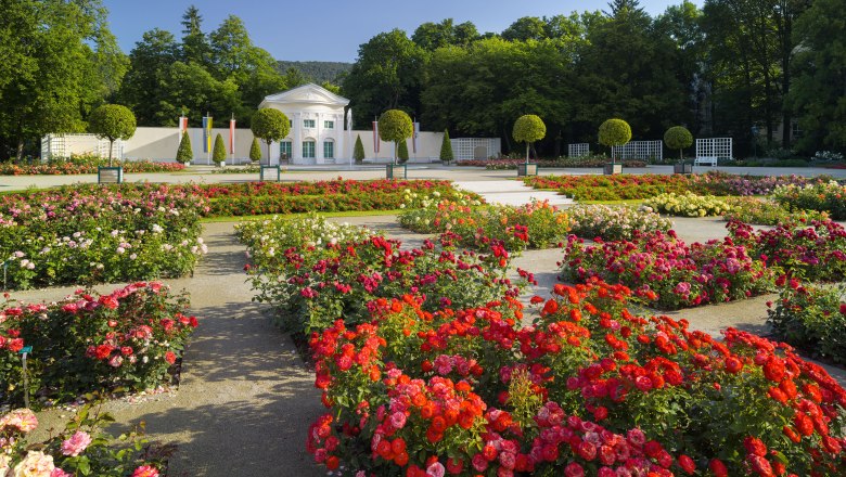 Ein Rosengarten mit bunten Blumenbeeten und einem weißen Pavillon im Hintergrund.